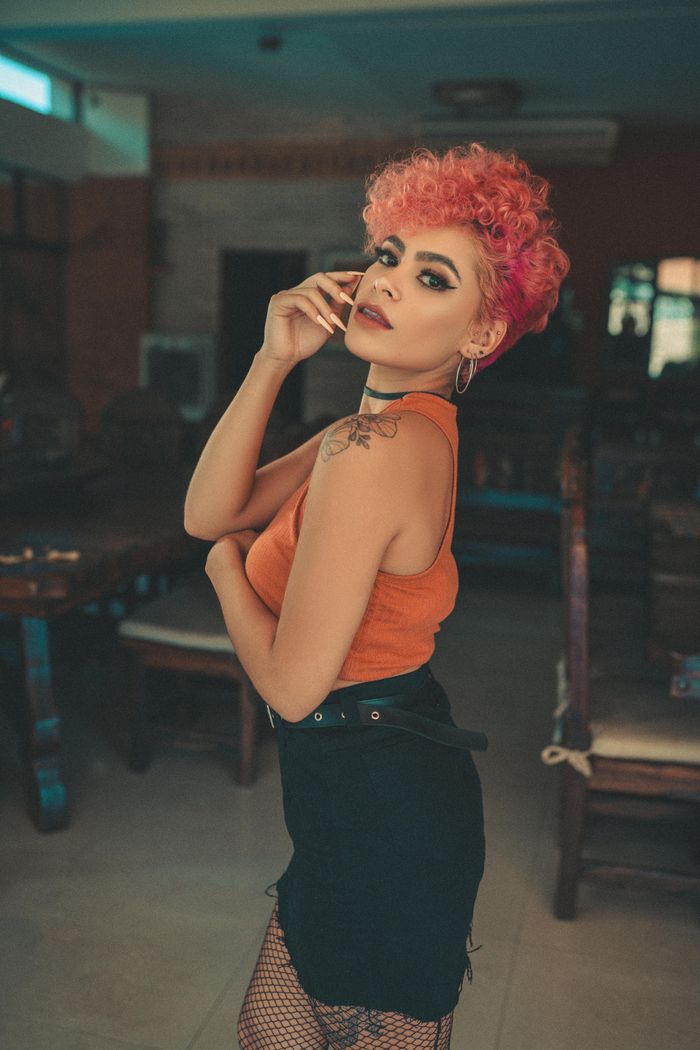 Vibrant portrait of a stylish woman with curly hair in an orange top and black skirt indoors.