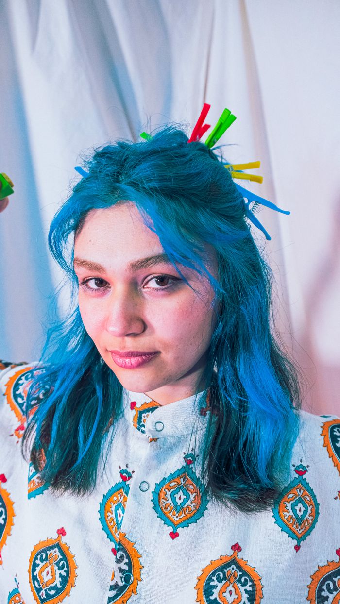Portrait of a woman with dyed blue hair and colorful accessories in a studio setting.