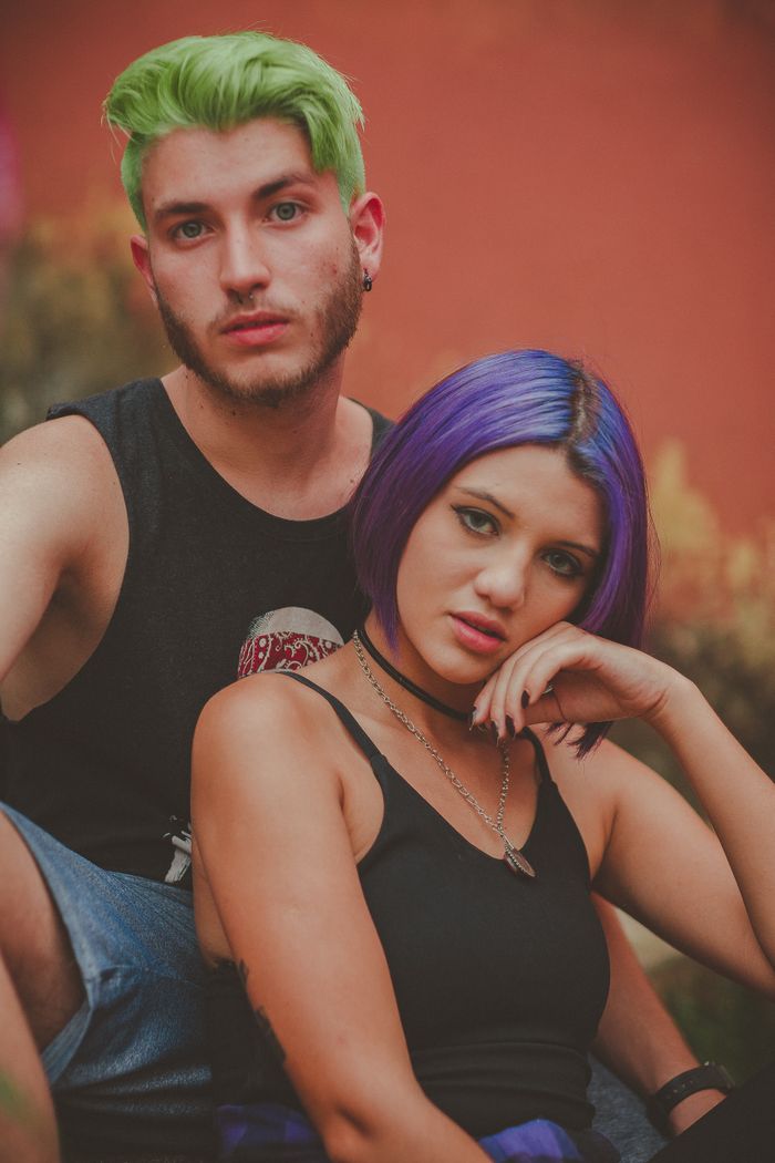 Vibrant portrait of two adults with trendy green and purple hairstyles, expressing unique style and fashion.