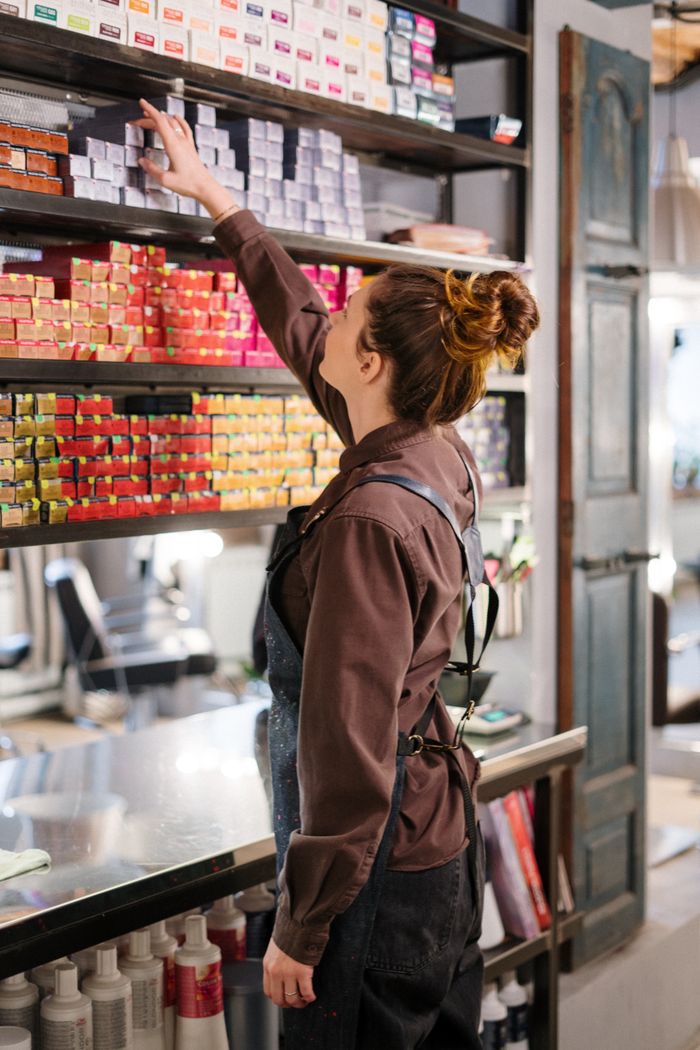 Hair stylist choosing hair color from organized salon shelves, focusing on preparation and profession.